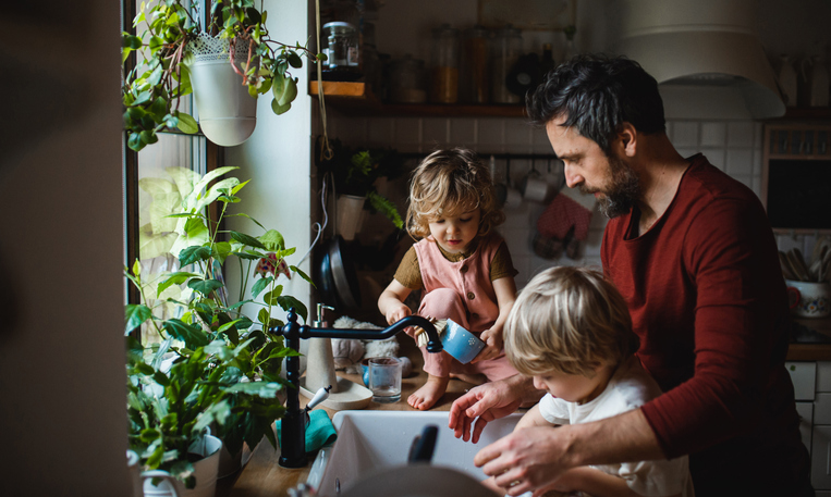 A mature father with two small children washing dishes indoors at home